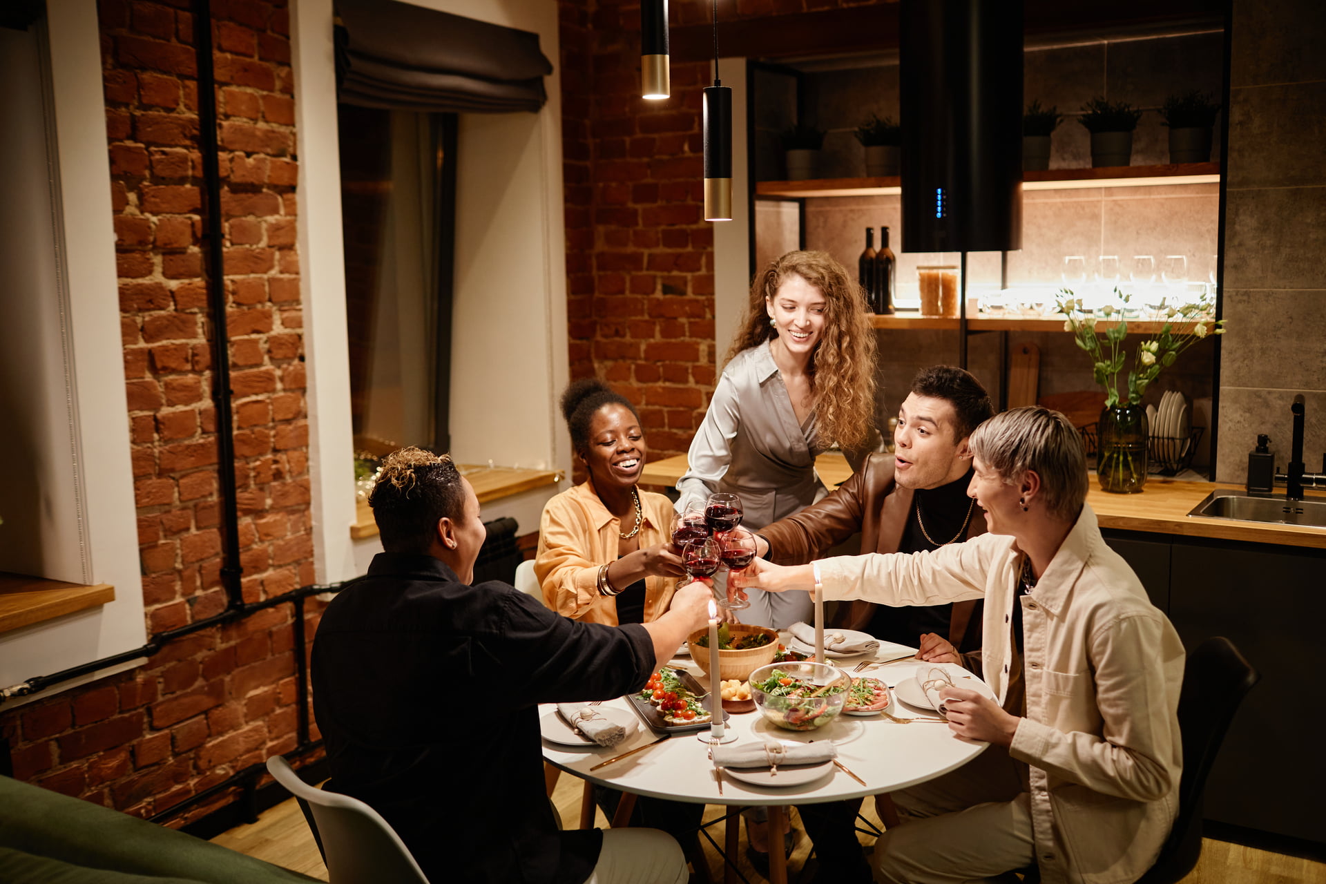 Group of young intercultural friends sitting by served table in the kitchen