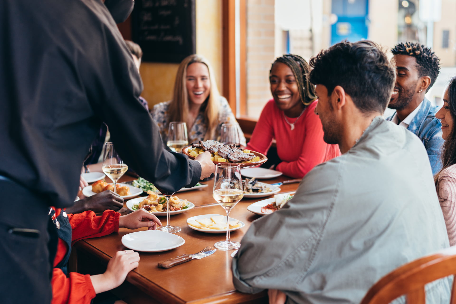 several customers of different ethnicities smile as a waiter serves them food
